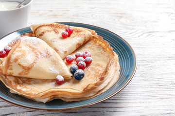 Thin pancakes served with sugar powder and berries on plate, closeup