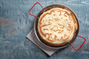 Dish with thin pancakes on wooden background, top view