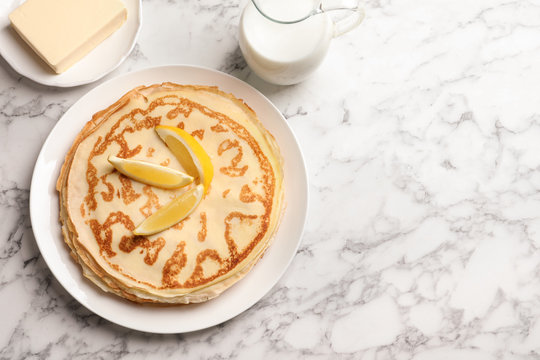 Thin pancakes with lemon, butter and milk on table, top view