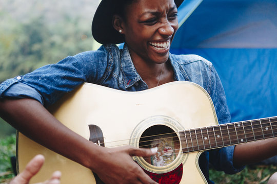 African American Woman Playing A Guitar At A Campsite