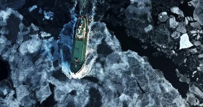 Flying above the Eastern Bosphorus strait. Aerial view of the ship slowly moving through ice floes. Others are stuck on the background. Vladivostok, Russia. Evening
