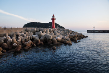 Red and white lighthouse at a seawall with wavebreakers in the deep bleue sea in Seogwipo, Jeju Island, South Korea