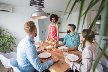 Friends in their 30's having a nice aperitif on a rustic wooden table in a lovely house. They are having fun and talking in front of glasses of white wine - real people