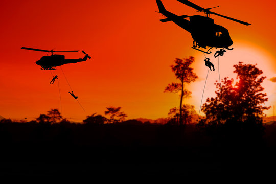 Silhouette Soldiers rappel down to attack from helicopter with sunset and copy space add text ( Concept stop hostilities To peace)