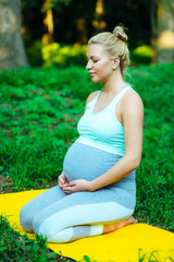 Fototapeta premium Pregnant girl sitting on a yoga mat in the park after training