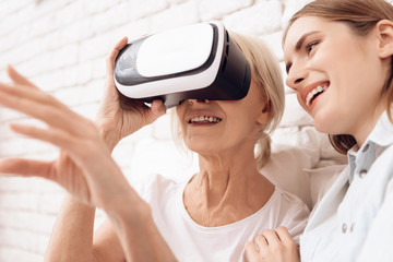 Close up. Girl is nursing elderly woman at home. They are using virtual reality.