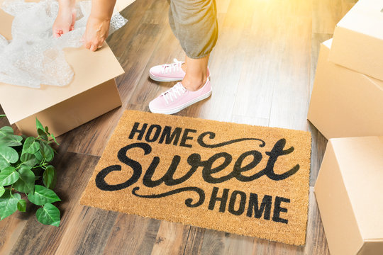 Woman in Pink Shoes and Sweats Unpacking Near Home Sweet Home Welcome Mat, Moving Boxes and Plant
