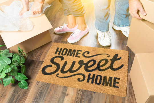 Man and Woman Unpacking Near Home Sweet Home Welcome Mat, Moving Boxes and Plant