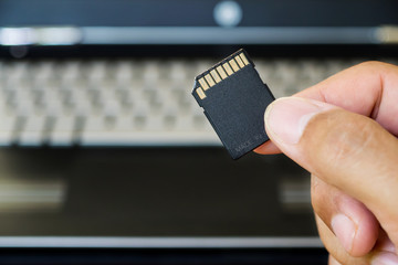 Hand holds SD Card against laptop pc.