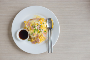 Omelette with pork bacon cutted on rice and sauce on white ceramic plate and spoon and fork