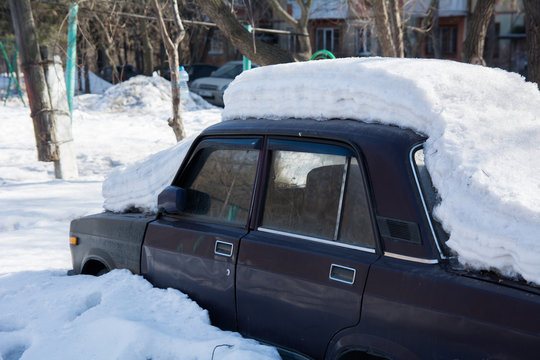 Old abandoned car covered with several layers of snow