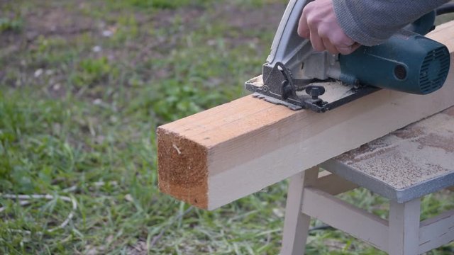 Hands sawing wooden beam lengthwise with a circular hand saw outdoors in summer