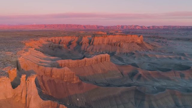 Aerial view flying over layers of cliffs lit up at sunrise near Factory Butte in the Caineville desert in Utah.