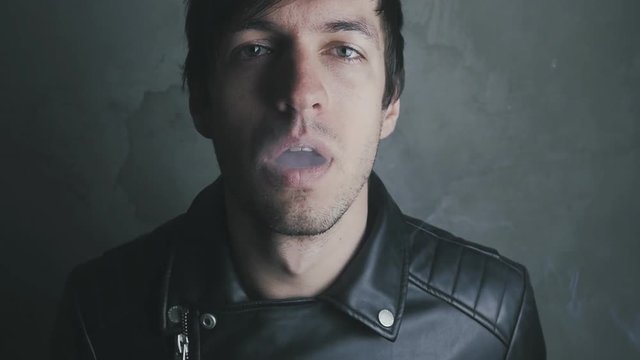 Young man in a leather jacket smokes a cigarette and drinks beer