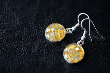 Resin earrings with yellow glitter on a dark background close up