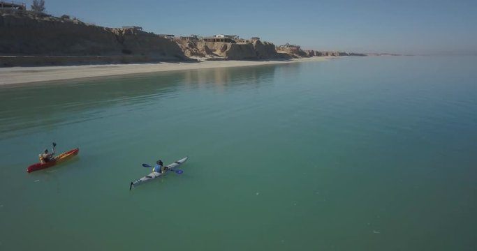 Aerial view of two women with a dog kayaking along a shoreline with steep cliffs