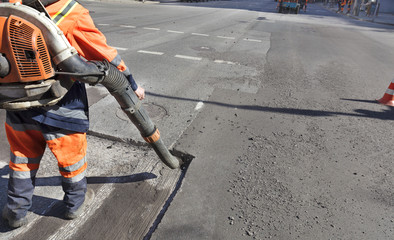 Partial repair of the asphalt road. The worker cleans the bad part of the road with an industrial...