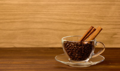 A glass cup with coffee beans and cinamon stics on wooden background with copyspace