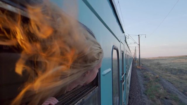 Woman riding train with blond hair blowing in the wind at sunset