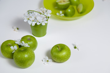 green apples in a plate and flowers in a small decorative pail