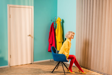 side view of pensive retro styled woman sitting on chair at bright apartment, doll house concept