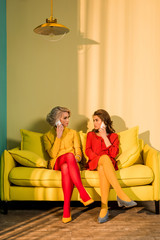 retro styled women talking on smartphones on yellow sofa, doll house concept