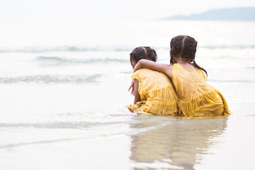 Back view of two cute asian little child girls hugging and having fun to play on beach together in summer vacation