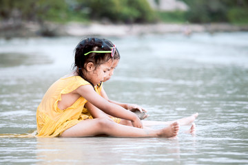 Two cute asian little child girls sitting and playing with sand on the beach together in summer vacation