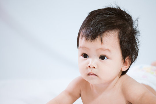 Cute asian baby girl wearing diaper lying on her stomach on the bed on white background
