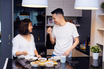 Young Asian couple cooking together while woman is feeding food to man at the kitchen. Happy couple and relationship concept