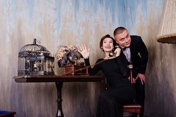 Fototapeta na wymiar Elegance woman in black evening dress with man in suit posed on studio near retro phone. Duet couple of two.