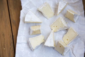 Pieces of round cheese brie or camembert in paper on wooden background. Closeup.