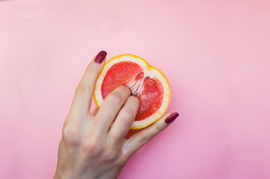 Two fingers on grapefruit on pink background. Sex concept.