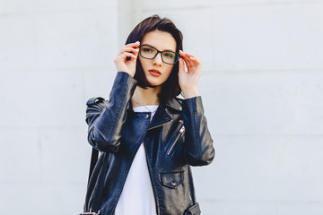 beautiful young girl in glasses in stylish clothes on light background outside