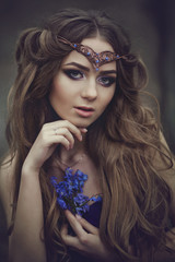 Portrait of a girl elf with long hair and blue eyes, wears a tiara with a bouquet of spring flowers in the forest. Girl Princess dreams.