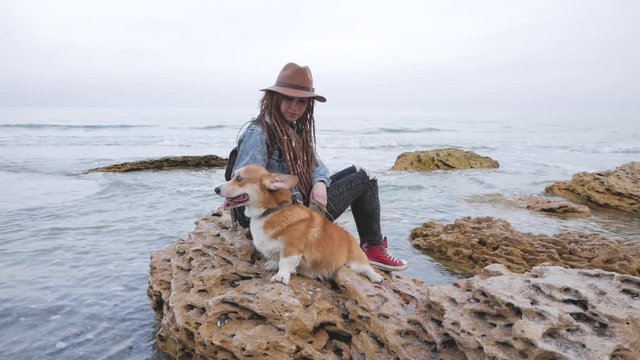 Young woman with corgi dog posing on the beach, girl with dreadlocks and hat with pet 