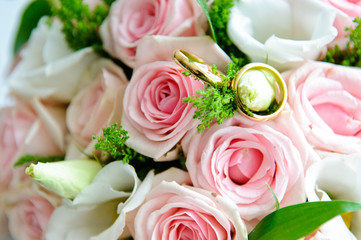 Gold wedding rings on a bouquet of the bride with pink roses.