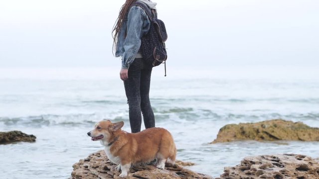 Young woman with corgi dog posing on the beach, girl with dreadlocks and hat with pet 