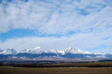 the landscape of the cloudy blue sky above the snow-capped peaks of the mountain range of the High Tatras in Slovakia.
