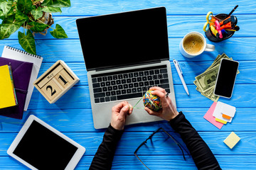 Business person tying rubber bands in ball by laptop on blue wooden table with stationery and money