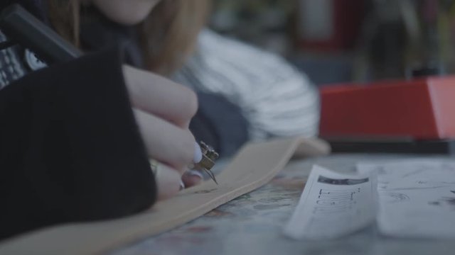 Woman uses a device for burning on natural leather. Creating and decorating of handmade wallet or bag. Close up view of artists working hands. 4k