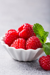 Fresh ripe raspberries in white bowl on light gray concrete background. Healthy food concept with copy space.