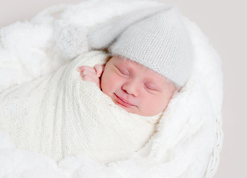 Newborn baby in white wrap laying on basket
