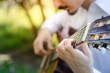 Young man with mustaches playing acoustic guitar in the park