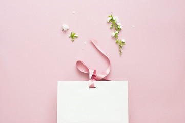 Flat lay top view White gift bag and spring flowers on a pink background. Greeting card with...