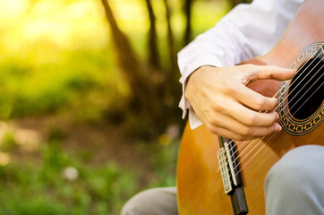 Hand of a man playing acoustic guitar in the park with sunlight