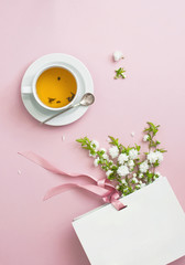 Obraz na płótnie Canvas Flatlay cup of tea, white gift bag and spring flowers on a pink background. Beautiful breakfast. Workspace pastel colors. Greeting card with delicate flowers Pink floral background