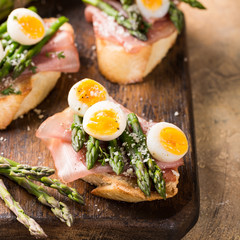 Fresh sendwich with ham, asparagus and quail eggs on old wooden chopping board. Easter spring breakfast concept.