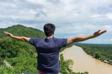 Fototapeta na wymiar young man happy and show to strength with hands rise up on beautiful river Landscape with beautiful cloudy sky