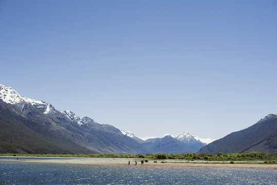 Paisaje de montañas con picos nevados frente a un lago. Escena diurna, cielo azul y despejado. Nueva Zelanda.	